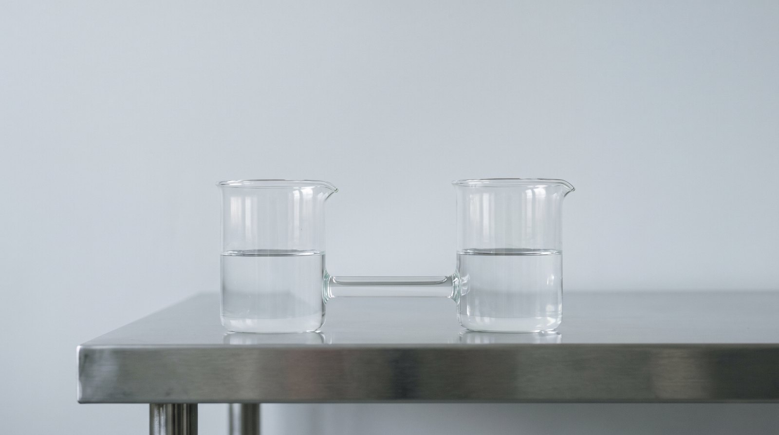 Dos vasos de cristal comunicantes con el agua al mismo nivel sobre una mesa, imagen que ilustra el préstamo socio sociedad y la valoración a valor de mercado